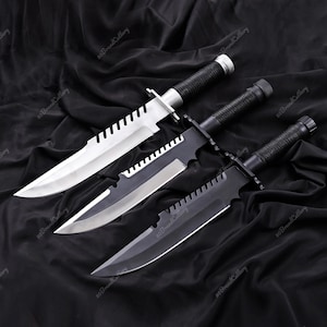 May include: Three survival knives with serrated blades and black handles are displayed on a black fabric. One knife has a silver blade, while the other two have black blades. The handles are textured for grip.