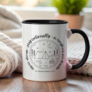 Puede incluir: Taza de cerámica blanca con interior y asa negros. La taza presenta un diseño circular con una tienda de campaña, árboles, luna y estrellas, con el texto "Rejoice always - pray continually - in everything give thanks" y "1ST THESSALONIANS 5:16-18".