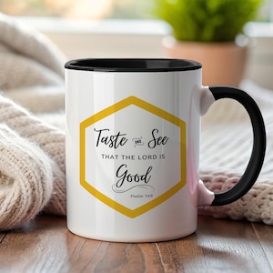 Puede incluir: Taza de cerámica blanca con interior y asa negros. La taza presenta un hexágono amarillo con el texto "Taste and See That The Lord Is Good" en escritura negra. El texto "Salmo 34:8" está debajo.