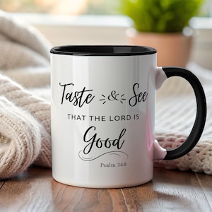 Puede incluir: Taza de cerámica blanca con interior y asa negros. La taza presenta el texto "Taste & See THAT THE LORD IS Good" en fuente negra, con "Psalm 34:8" debajo. La taza está sobre un fondo neutro.