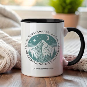 Puede incluir: Taza de cerámica blanca con interior y asa negros. La taza presenta un diseño de montaña y luna turquesa con las palabras "Dad gracias en todo" y "1 Tesalonicenses 5:16-18".