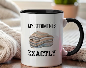 May include: White ceramic mug with a black interior and handle. The mug displays the text "MY SEDIMENTS EXACTLY" and an illustration of a layered rock formation. The mug is set against a neutral background.