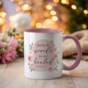 Puede incluir: Taza de cerámica blanca con interior y asa rosas. La taza presenta el texto "And by His wounds we are healed" en un diseño floral. También se incluye el texto "Isaiah 53:5".