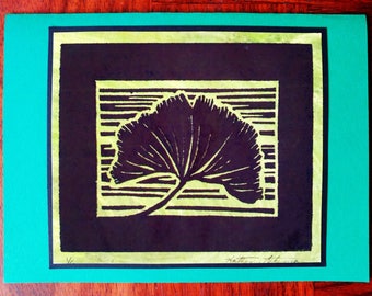 May include: A black and green print of a ginkgo leaf on a white background. The print is framed in a black and green frame. The artist's signature is in the bottom right corner.