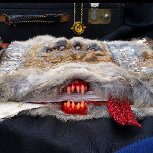 May include: A book with a furry, gray and brown cover with a toothy, red mouth and a red tongue sticking out. The book has a brown leather strap with a buckle.