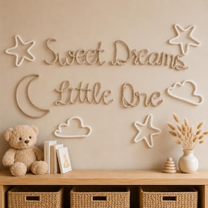 May include: Wall decor featuring the text Sweet Dreams Little One in tan rope, accompanied by white rope shapes of two stars, a crescent moon, and two clouds. A tan teddy bear, books, and a vase with dried grass sit on a wooden shelf.
