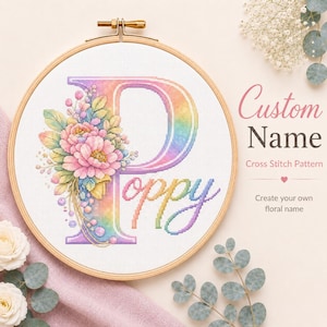 May include: A cross-stitch hoop featuring a floral design with the name "Poppy" in a rainbow gradient. The letter "P" is decorated with pink and yellow flowers and green leaves. The text "Custom Name" and "Cross Stitch Pattern" are also visible.