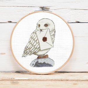 May include: White owl with a letter in its beak, sitting on a rock. The owl is holding a white envelope with a red wax seal.