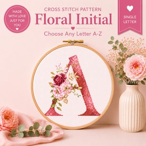 Può includere: Un modello a punto croce con la lettera "A" ornata da elementi floreali rosa e bordeaux, presentato in un telaio da ricamo in legno. Il testo include "Floral Initial" e "Choose Any Letter A-Z".