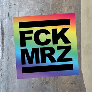 Könnte beinhalten: Ein quadratischer Aufkleber mit regenbogenfarbenem Hintergrund und dem fetten schwarzen Text FCK MRZ, der zwischen zwei dicken schwarzen horizontalen Linien zentriert ist. Der Aufkleber klebt auf einer strukturierten grauen Fläche.
