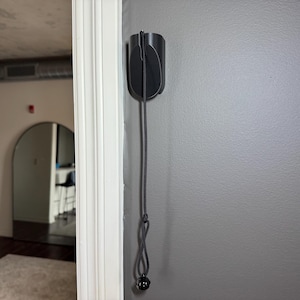 May include: A black wall mount with a black cord hanging down. The cord has a black ball at the end.