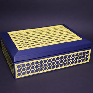 May include: A rectangular blue box with a yellow, perforated top and decorative yellow trim. The box has a geometric pattern on the sides and a contrasting colour scheme, creating a modern aesthetic.