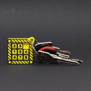 May include: A yellow and black key chain with a numerical keypad design, displaying the numbers 2, 3, 1, 5, 6, 4, 7, and 8. The key chain is attached to a set of keys with black and silver key heads.
