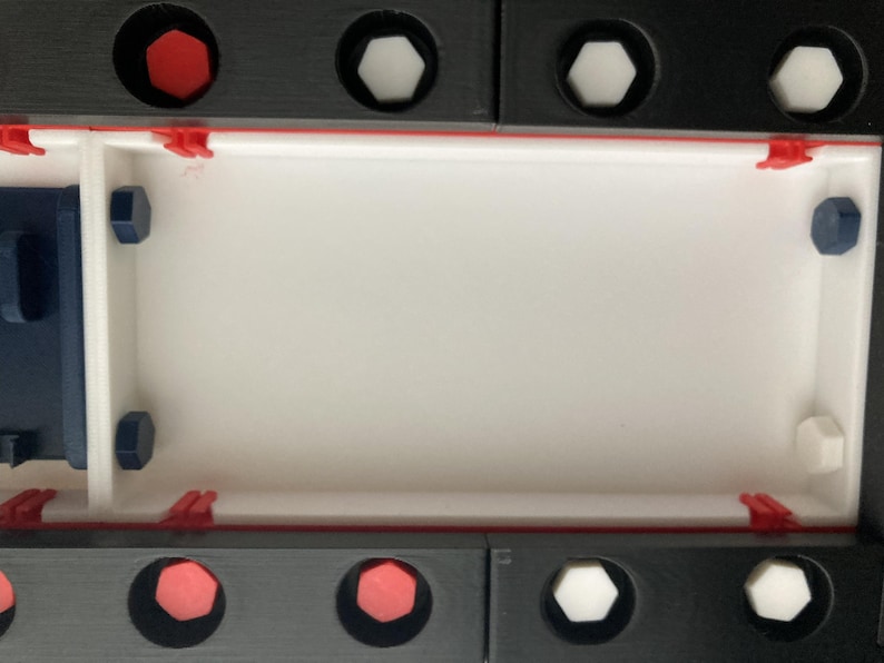 May include: A rectangular, modular construction set with a white interior and black exterior. The set features red, white, and blue accents, including hexagonal and circular elements, and red clips. The design is geometric and modern.