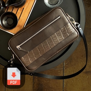 May include: A brown leather crossbody bag with a zipper closure and a crocodile-embossed design. The bag has a black strap and silver hardware.