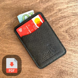 May include: A dark green leather card holder with a stitched edge and a kangaroo logo. The text "Suri Leather" is embossed on the holder. A red credit card and a ten euro bill are visible in the pocket.