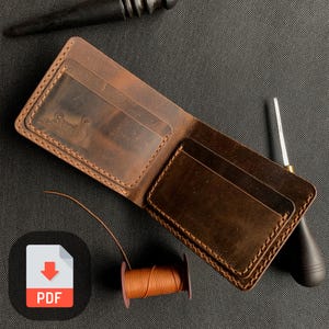 May include: A brown leather wallet with multiple card slots and a stitched edge. The wallet is lying on a dark gray surface with a spool of orange thread and a leather awl.