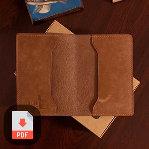 May include: A brown leather wallet with two card slots and a pocket for cash. The wallet is open and the inside is visible. The wallet has the word "Suri" printed on the front.