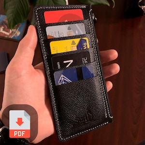 May include: Black leather wallet with white stitching and a zipper. The wallet has four card slots and is holding multiple cards. The wallet has a small logo on the front.
