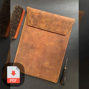 Puede incluir: Una funda para portátil de cuero marrón con cierre de solapa. La funda tiene un aspecto desgastado y está hecha de cuero de alta calidad.