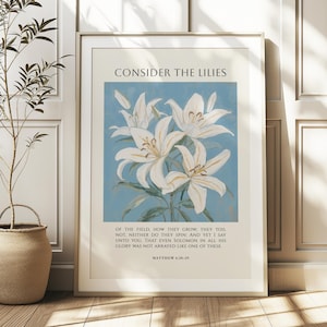 Może przedstawiać: Oprawiony wydruk artystyczny z kwiatową ilustracją białych lilii na jasnoniebieskim tle. Tekst "CONSIDER THE LILIES" znajduje się na górze, poniżej werset biblijny. Wydruk jest w złotej ramie.
