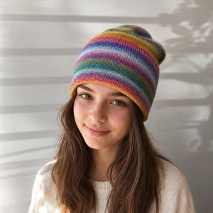 May include: A knit beanie featuring a vibrant, multi-colored horizontal striped pattern in shades of yellow, orange, red, purple, blue, and green. The hat has a soft, textured appearance with a snug fit around the head, showcasing a gradient effect.