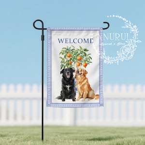 May include: A garden flag with a blue and white border features the word "WELCOME" above a watercolor illustration. The illustration depicts a tree with oranges and two dogs, a black dog and a golden retriever.