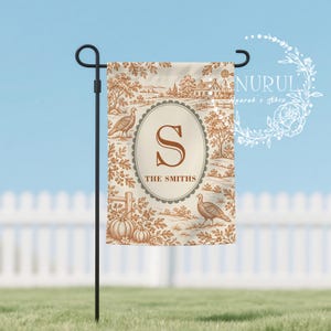 May include: A rectangular garden flag hanging on a black metal stand, featuring a brown and cream toile-style print of turkeys, pumpkins, and rural scenery. A central oval frame contains the letter S and the text THE SMITHS in brown font.