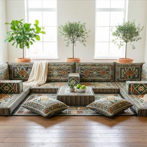 May include: A modular sofa set with patterned cushions and a matching rug. The design features geometric patterns in green, brown, and orange. Decorative plants in terracotta pots and a small table with fruit complete the scene.