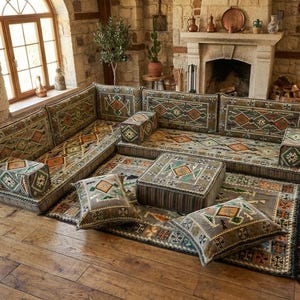 Peut inclure: Un ensemble de salon avec un motif dans les tons de marron, vert et orange. L'ensemble comprend un canapé d'angle, un tapis, deux poufs et plusieurs coussins. Le mobilier est posé sur un sol en bois.