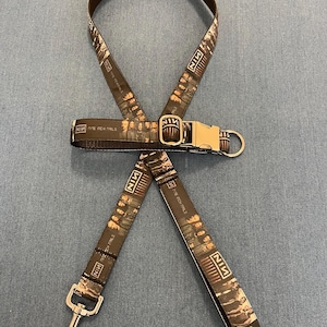May include: A brown dog leash with a black and white printed design featuring the band Nine Inch Nails. The leash has a metal clip and a metal ring.