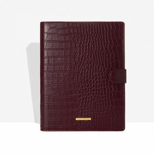 May include: A burgundy faux-leather journal with a crocodile skin texture. The journal has a flap closure and a small gold-colored rectangular label at the bottom. The journal is closed and appears to be new.
