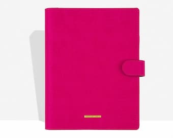 May include: A bright pink, rectangular journal or planner with a magnetic closure. The cover is a solid, vibrant pink with a small, rectangular gold-colored accent near the bottom. The journal is closed and upright.