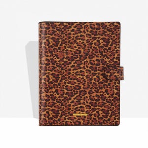 Puede incluir: Un diario con estampado de leopardo marrón y negro, con cierre de botón a presión. El diario tiene una etiqueta dorada en la parte inferior. La cubierta es un patrón repetido de manchas marrones y negras.