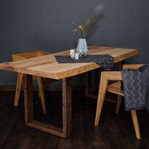 Könnte beinhalten: Ein Esstisch aus hellem Holz mit natürlicher Kante, kombiniert mit passenden Stühlen. Auf dem Tisch befinden sich eine Vase mit Blumen, Kerzen, ein gemusterter Tischläufer und eine graue Decke. Der Tisch ist etwa 180 cm lang.