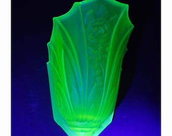 May include: A vibrant neon green glass wall sconce shade featuring a molded floral relief pattern. The translucent glass emits a bright glow, showcasing vertical ridges and a scalloped top edge with a rounded base, illuminated under UV light.