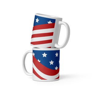 May include: Two white ceramic mugs stacked vertically, each featuring a graphic print of the American flag. The design includes a blue field with white stars and alternating red and white horizontal stripes wrapping around the exterior surface.