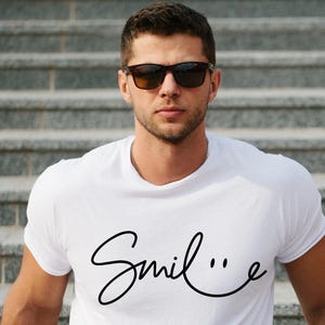 May include: A white t-shirt with a black cursive font that says "Smile..." with a smiley face at the end of the word.