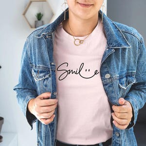 May include: A pink t-shirt with the word "Smile" written in cursive with a smiley face at the end of the word.
