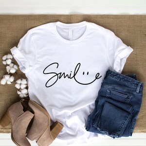 May include: White t-shirt with the word "Smile" written in a cursive font with a smiley face at the end of the word.