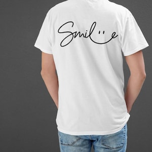 May include: White t-shirt with a black cursive "Smile" design on the back. The design includes a smiley face.