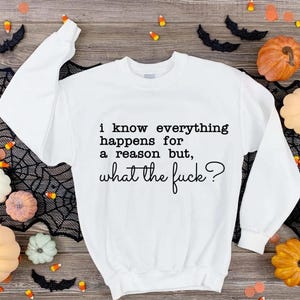 以下が含まれることがあります： 「I know everything happens for a reason but, what the fuck?」のテキストが入った白いスウェットシャツ。画像はカボチャ、コウモリ、クモの巣、キャンディーコーンで飾られており、ハロウィーンに最適です。