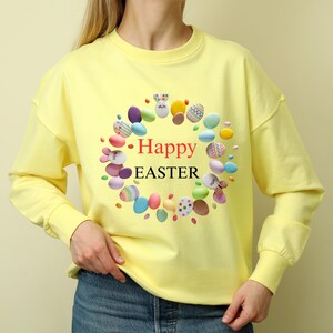 May include: Yellow sweatshirt with a colorful Easter egg wreath design and the text "Happy Easter".