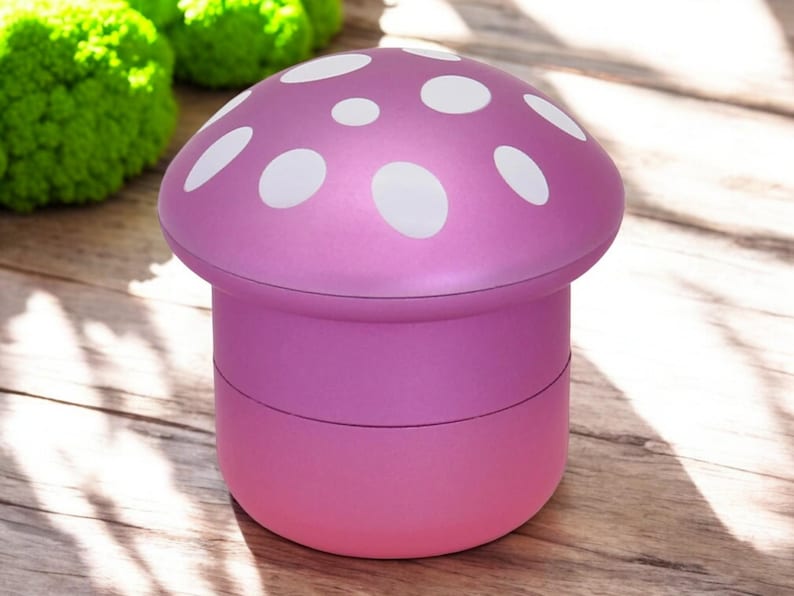 Pink mushroom-shaped grinder with white polka dots, shown closed on a wooden surface with a natural light background – a cute and funny 4-piece spice grinder for herbs, ideal as a gift or kitchen accessory.
