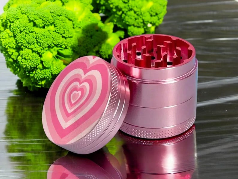 Cute pink aluminum grinder with heart design, durable 4-piece setup with catcher, designed as a stylish grinder for women or stoner gift idea.