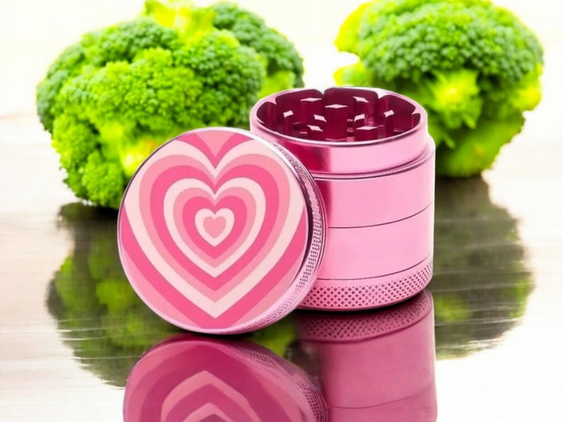 Stylish pink herb grinder with a heart design, featuring sharp teeth for easy grinding; ideal girly grinder or stoner gift.