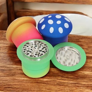 Colorful mushroom grinders in green, blue, and red-yellow gradients displayed on a wooden table, showing sharp metal teeth and pollen screens – cute and funny 4-piece spice grinders for herbs and seasonings.