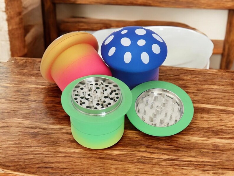 Colorful mushroom grinders in green, blue, and red-yellow gradients displayed on a wooden table, showing sharp metal teeth and pollen screens – cute and funny 4-piece spice grinders for herbs and seasonings.