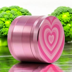 Closed pink 4-piece grinder with heart design, sleek aluminum build, great for grinding herbs or spices; beautiful and functional stash accessory for her.