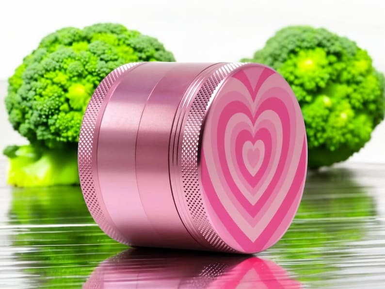 Closed pink 4-piece grinder with heart design, sleek aluminum build, great for grinding herbs or spices; beautiful and functional stash accessory for her.